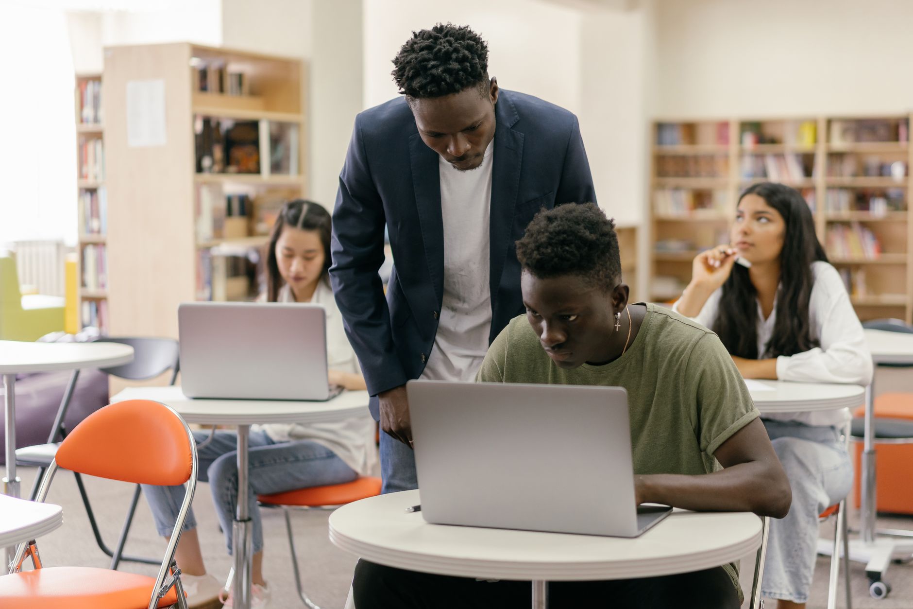 A teacher helping students working on laptops in a classroom