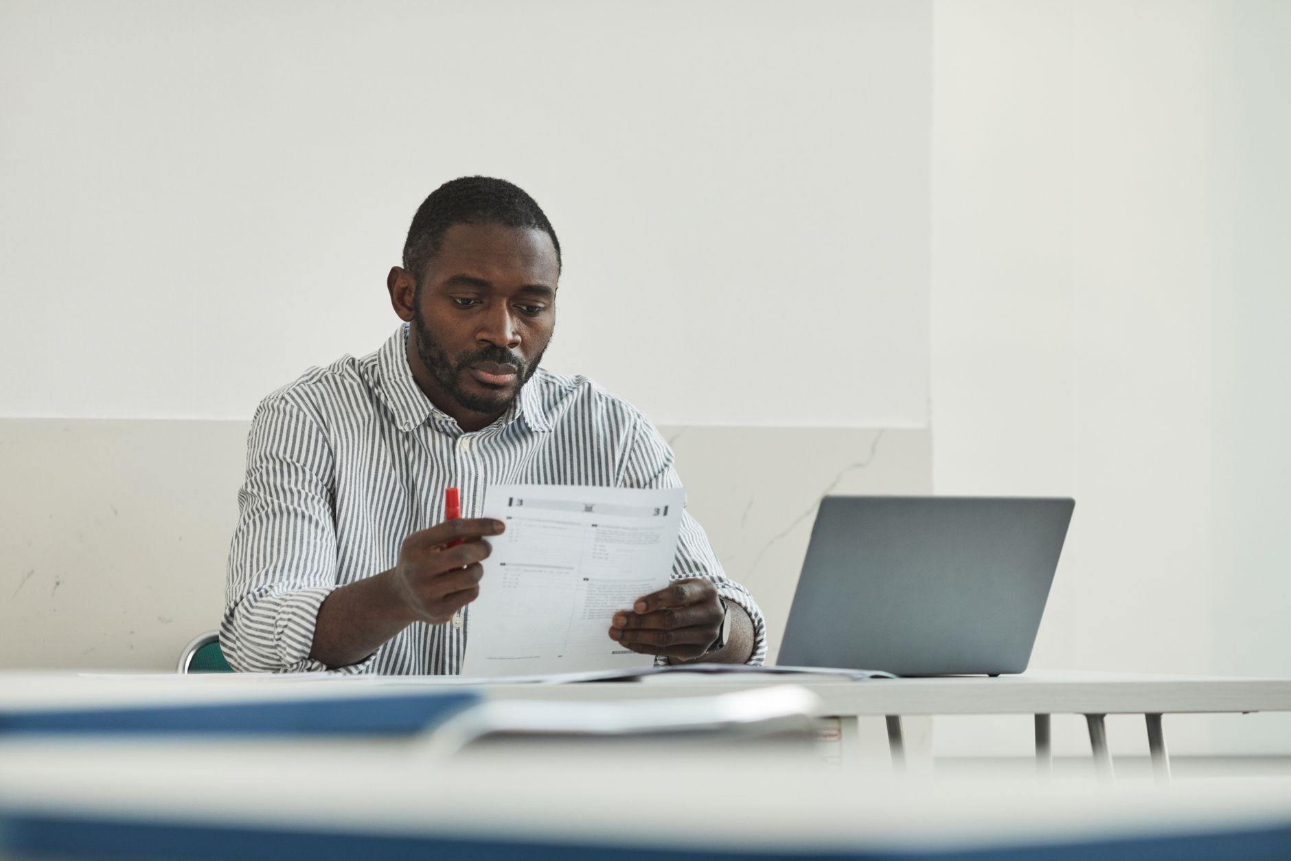A teacher reviewing a marked test paper next to a laptop