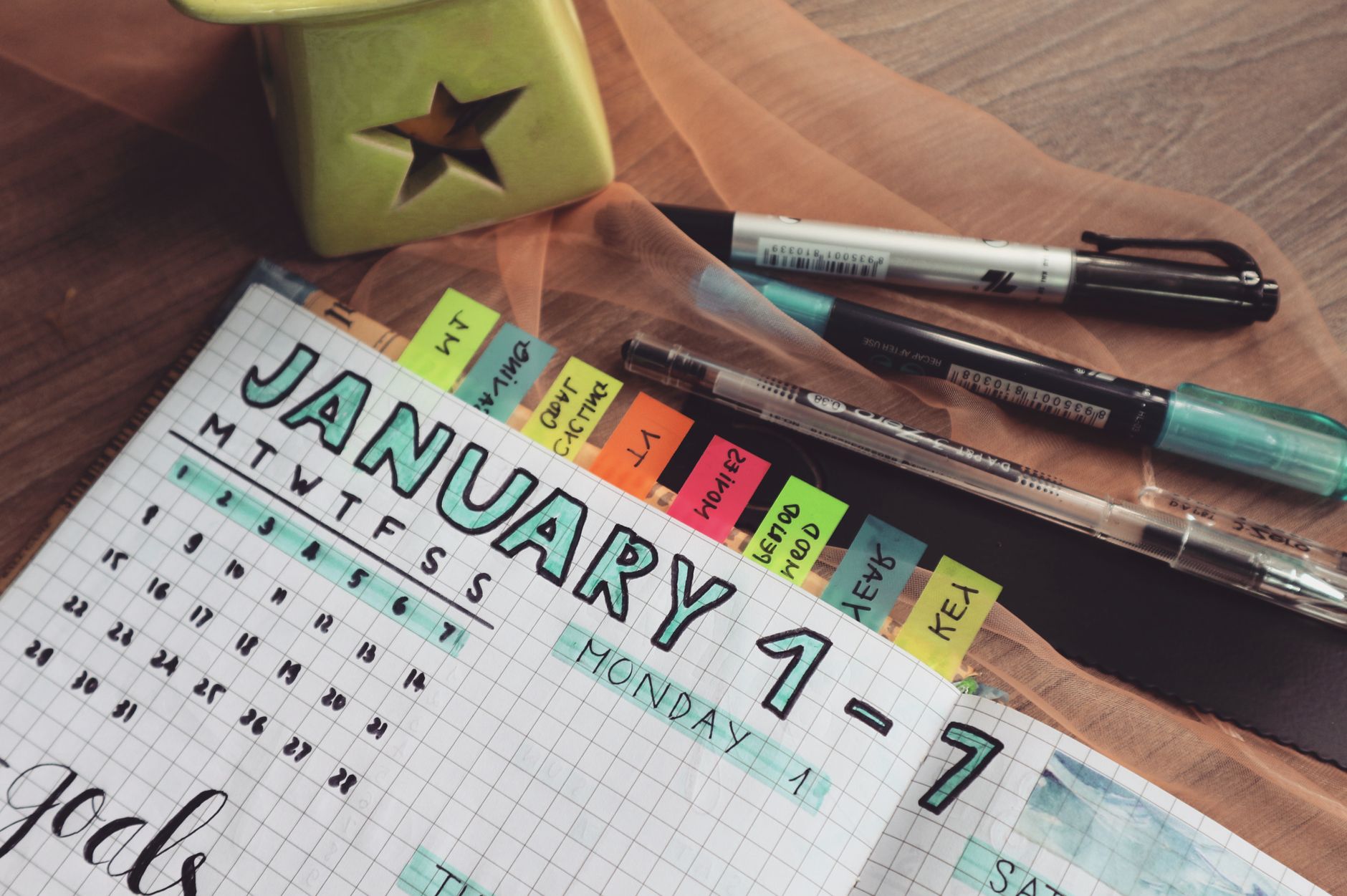 A hand-drawn weekly planner layout in a grid notebook with pens