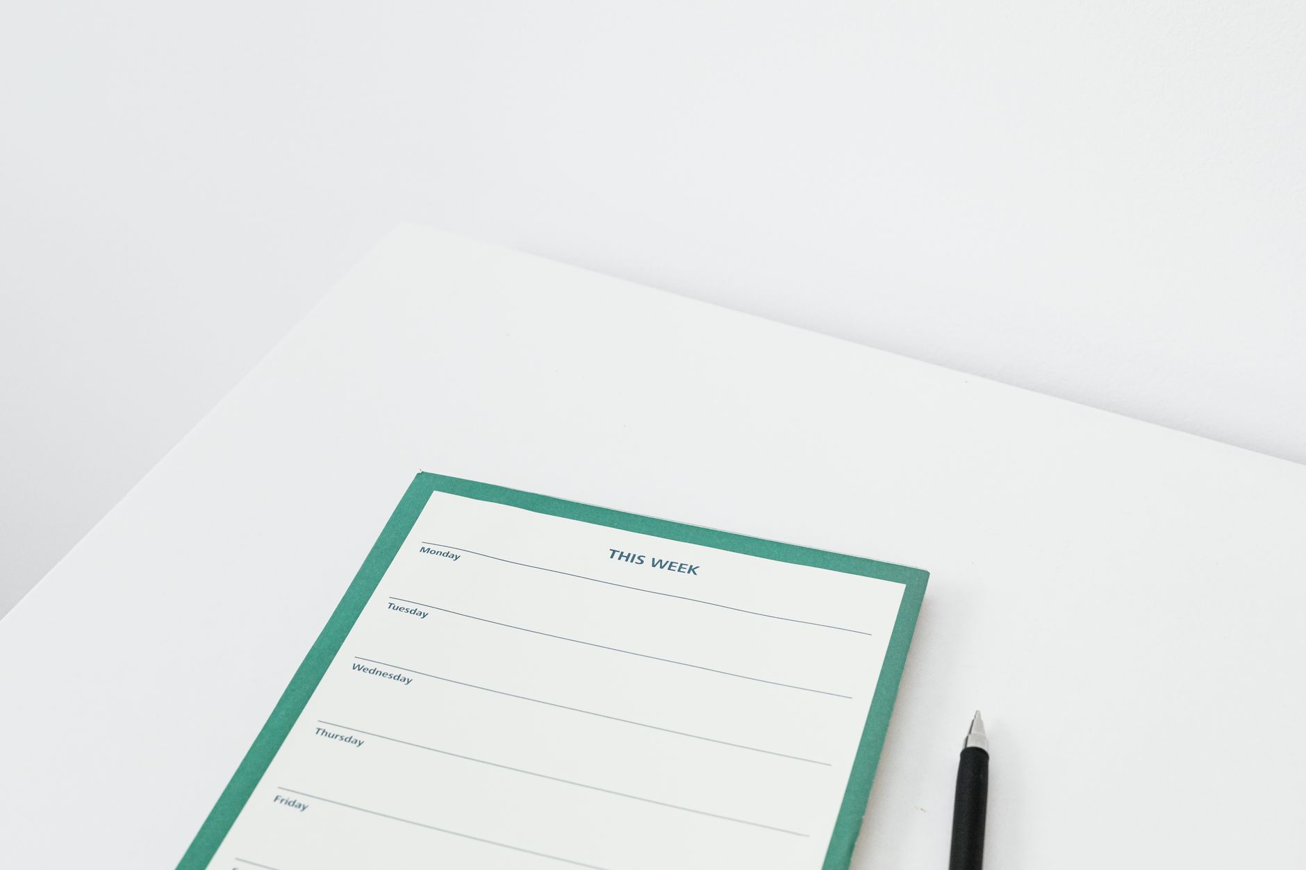 A weekly planner notepad with a pen on a white desk