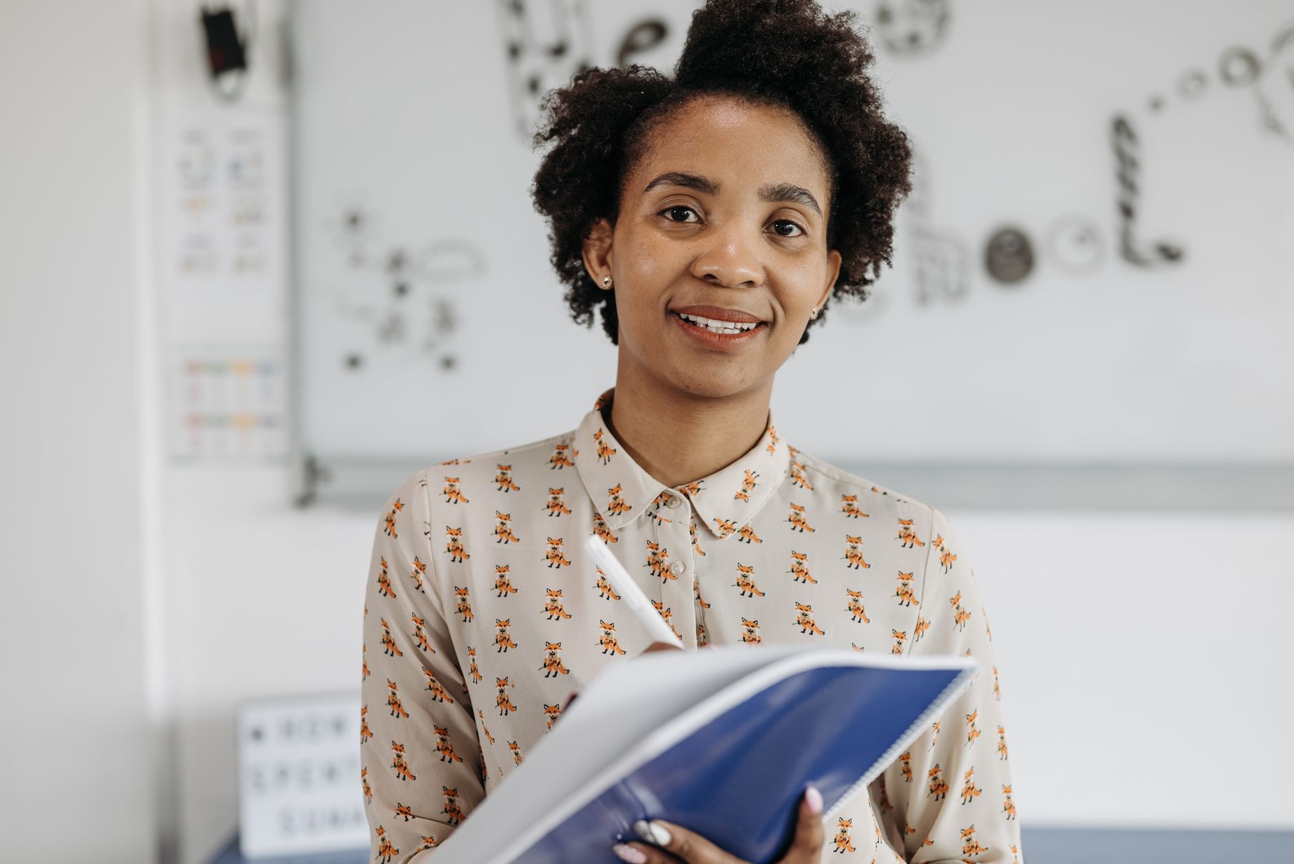 A teacher smiling while writing notes in a notebook