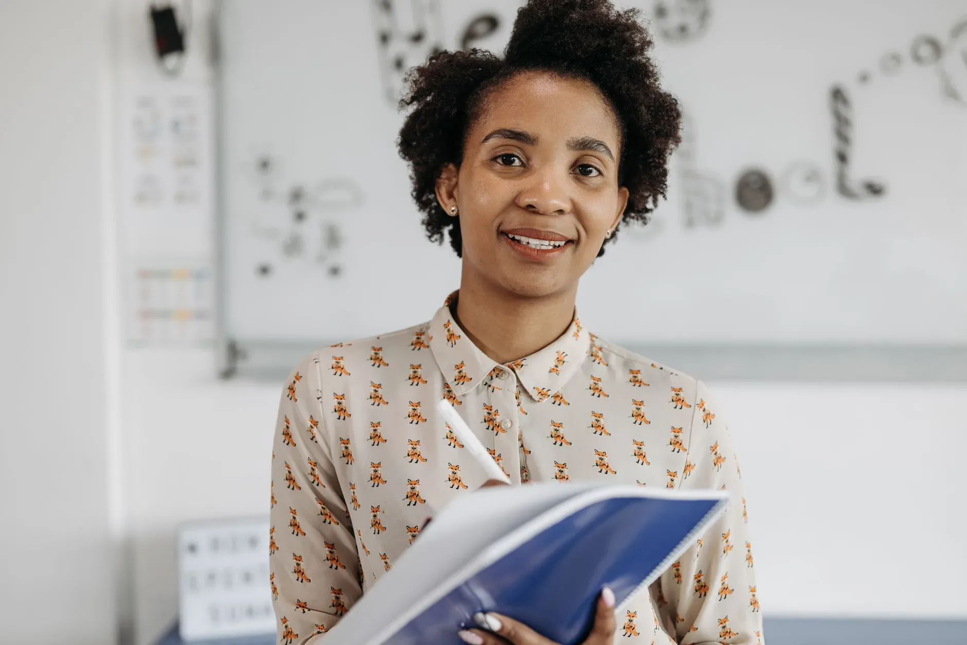 A teacher smiling while writing notes in a notebook